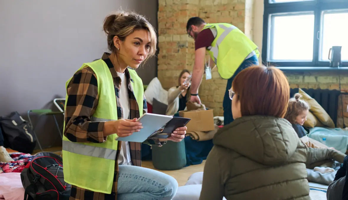 Volunteer wearing a bright neon vest sitting with a person whose face is turned away from viewer